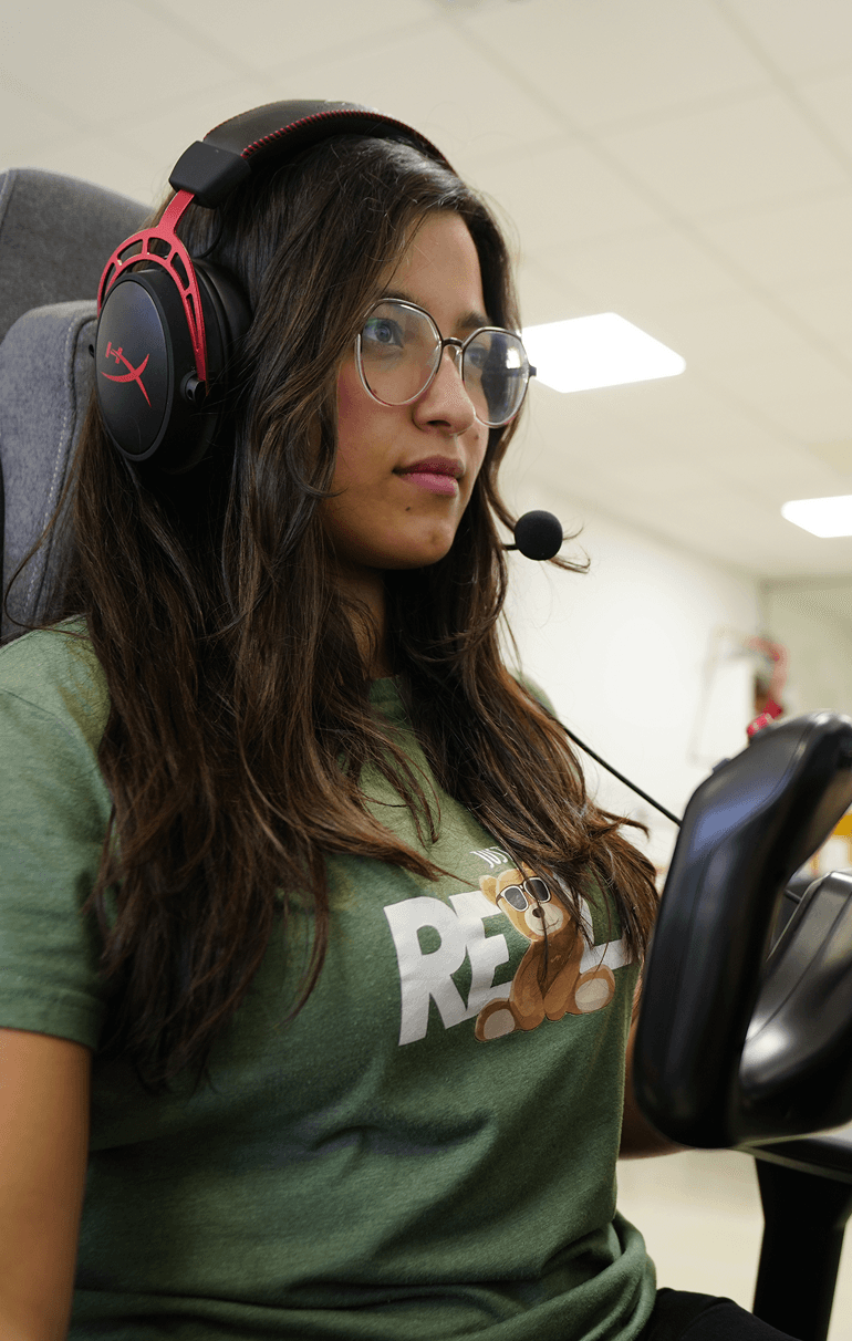 A student wearing  a headset focuses on a computer screen while gaming or working on a simulation